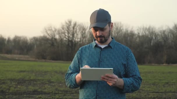 Un granjero con una tableta en un campo sonriendo, un agran trabajando en la tierra, cultivando verduras y frutas, un hombre escribiendo en la pantalla de un gadget, 4K — Vídeo de stock