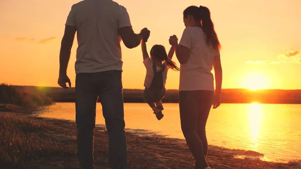 Małe dziecko trzyma mamę i tatę za rękę przy zachodzącym słońcu. Dzieciństwo z rodzicami o świcie. Szczęśliwego życia rodzinnego. Matka, ojciec i dziecko w blasku słońca. Podróż wzdłuż plaży, w pobliżu wybrzeża — Zdjęcie stockowe
