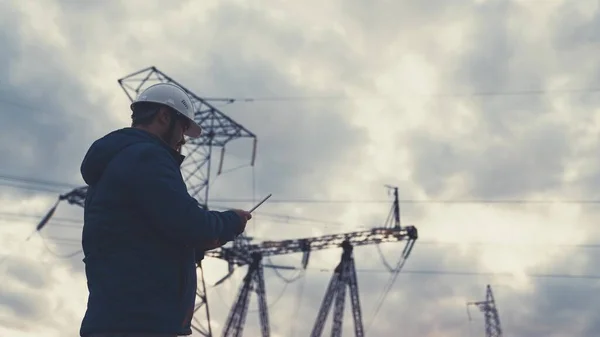 Elektrik hatlarının yakınında tabletle çalışan kıdemli elektrik mühendisi. Kıdemli elektrik mühendisi elektrik enerjisi dağıtır. Bir tabletle elektrik enerjisiyle çalışan iş adamı elektrikçi. — Stok fotoğraf