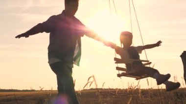 Oyuncak ayısı ve babası olan mutlu bir çocuk gün batımında parkta salıncakta salıncak sürüyor ve havada uçan uçağı çalıyor. Kızları ve babaları şafakta eğleniyorlar. Mutlu aile hayatı konsepti. Çocuk