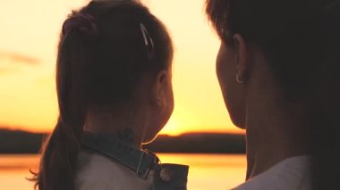 Mutlu anne ve küçük kız gün batımında gökyüzünde kucaklaşıp gülümsüyor, mutlu aile kavramı, anne ve çocuk şafakta buluşuyor, macera ve açık havada oyunlar oynuyor, ebeveynler sevgili çocukla tatil yapıyor.