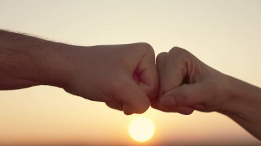 Gün batımında gökyüzünde takım çalışması konsepti. Yumruk yumruğa dayanışma, saygı ve kardeşlik jesti. Yaşam tarzı iş adamları yumruklarını yakın plan çekiyorlar. Farklı ortaklık ilişkileri olan insanlar.