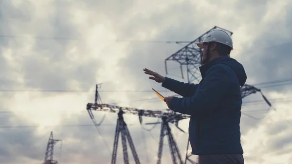 Senior electrical engineer working with tablet near electrical lines. Senior electrician engineer distributes electrical energy. Businessman electrician working with electrical energy with a tablet