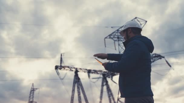 Senior elingenjör som arbetar med surfplatta nära elledningar. Överordnad elektriker ingenjör distribuerar elektrisk energi. Affärsman elektriker arbetar med elektrisk energi med en tablett — Stockvideo