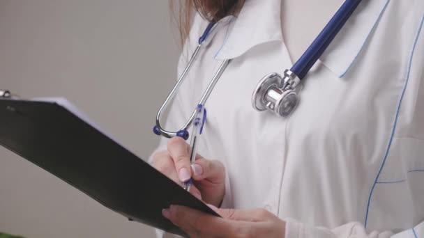 Un médecin en blouse blanche avec un stéthoscope rédige une ordonnance dans une tablette avec un stylo, les services médicaux d'un thérapeute spécialiste, le traitement des personnes au travail, concept d'entreprise, 4K, gros plan — Video