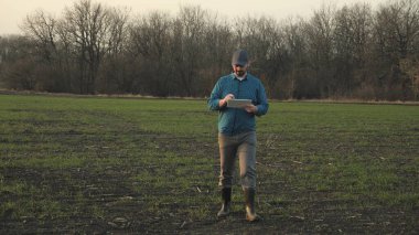 Tarlada elinde tabletle dolaşan bir çiftçi, yerde iş tarımcısı, sebze ve meyve yetiştirme konsepti, kırsal alanda yaşam, istihdam.
