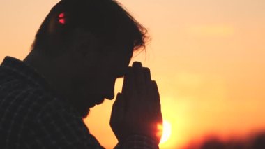 Dua eden adam, gün batımında ellerini dua siluetine sardı. Yavaş çekim video yaşam tarzı, adam ellerini kavuşturup dua ediyor, Tanrı 'ya dua ediyor, tövbe günahları için af diliyor, inanan adam.