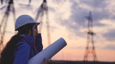 Kask siluetindeki elektrik mühendisi güneş batımında kulenin yanında elektrikle çalışıyor. İş enerjisi teknoloji endüstrisi konsepti. Elektrikçi yaşam tarzı üzerine okuma belgeleri okuyor