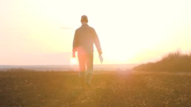 Ziraat. Akıllı tarım teknolojisi. Çiftçi, gün batımında yeşil çimlerde dijital tabletle botlarla yürüyor. Çiftçilik tarım kavramı