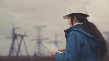 Elektrik hatlarının yakınında tabletle çalışan kıdemli elektrik mühendisi. Kıdemli elektrik mühendisi elektrik enerjisi dağıtır. Bir tabletle elektrik enerjisiyle çalışan iş adamı elektrikçi.