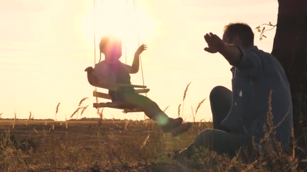 Father shakes his little daughter on a swing in the glare of the sun, dad and kid play samlet at sunset, soar in the air and fly in the game, man greets dawn with child, travel family life concept — Stock Video