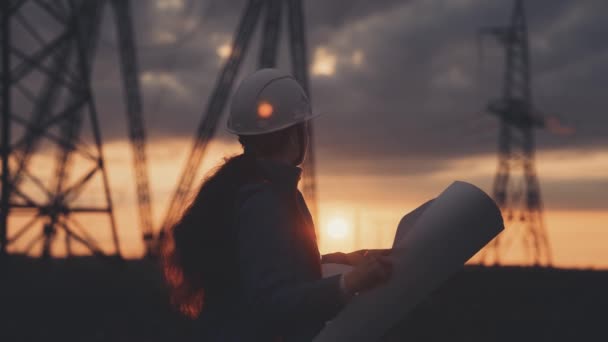 Elektrotechniker in Helm-Silhouette arbeitet bei Sonnenuntergang in der Nähe des Turms mit Strom. Business Energy Technology Branchenkonzept. Elektriker studiert Lektüre von Dokumenten zum Lebensstil — Stockvideo