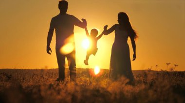 Gökyüzünde gün batımında özel bir ailenin silueti, anne, baba ve çocuk açık havada yürüyor, kız şafakta anne ve babanın kollarında uçuyor, akşam güneşin parlaklığında güzel bir şekilde seyahat ediyor.