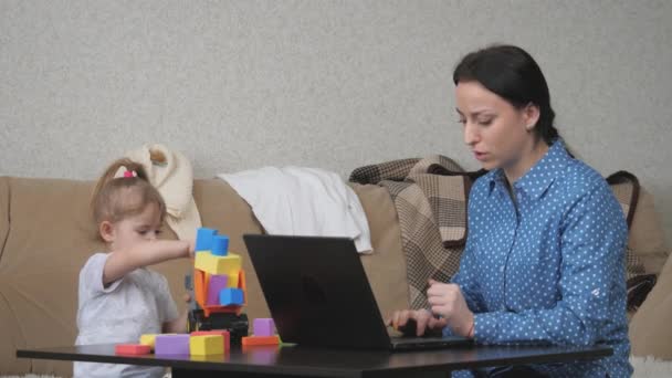 Una mujer independiente trabaja en una computadora en casa de forma remota con un niño pequeño, mamá hace un pedido en una tienda en línea a través de una aplicación para computadora portátil, tecnologías modernas de sistemas de gatget en una vida de personas — Vídeo de stock