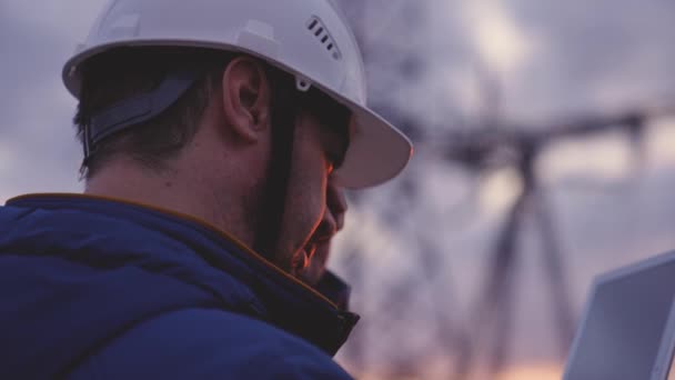 Silueta de ingeniero de pie en el campo con torres eléctricas. Ingeniero eléctrico con pilón eléctrico de alto voltaje al atardecer. Trabajadores del poder en el trabajo concepto — Vídeo de stock