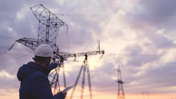 Elektrik kuleleri olan bir mühendis silueti. Günbatımı arka planında yüksek voltajlı elektrik pilonu olan elektrik mühendisi. İş konseptinde elektrik işçileri