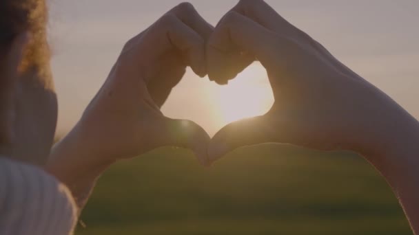 Porträtt av en flicka från händerna gjorde en hjärtform vid solnedgången, mot en orange bakgrund. Begreppet: kärlek till avkoppling, frihet, kärlek, livsstil, kväll solnedgång, sommar, sol. — Stockvideo