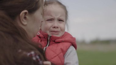 Anne bebeği sakinleştirir. Çocuk parkta annesinin kollarında ağlıyor. Gözlerinde yaşlarla aile annesi ve çocuğu annelerine duygusal olarak sarılıyorlar. Sevgi dolu genç bir anne küçük kızını kucaklıyor ve sakinleştiriyor.