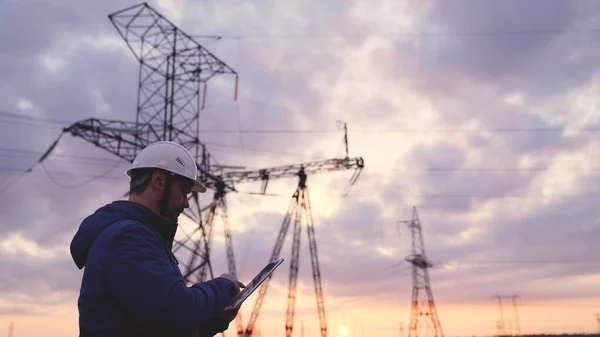Elektrik kuleleri olan bir mühendis silueti. Günbatımı arka planında yüksek voltajlı elektrik pilonu olan elektrik mühendisi. İş konseptinde elektrik işçileri