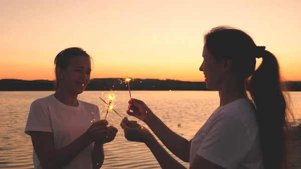 Las chicas felices prenden fuego a los bengalas al atardecer en el cielo y se ríen. Los jóvenes saludan al amanecer con hermosas luces. Las novias viajan. Descanse durante las vacaciones. Celebrando tu cumpleaños con diversión —  Fotos de Stock