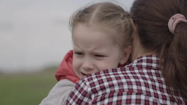 A mamã acalma o bebé. criança está chorando no parque nos braços da mãe. família mãe e filho com lágrimas nos olhos abraça sua mãe, emocionalmente. amando jovens abraços de mãe e acalma sua filhinha — Fotografia de Stock