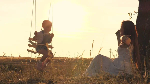 Gelukkige moeder schudt het kleine kind hoog op de schommel, het kind ervaart het gevoel van vliegen tijdens het spelen met zijn moeder, hoog van de grond naar de hemel, het concept van een gelukkig gezinsleven — Stockfoto