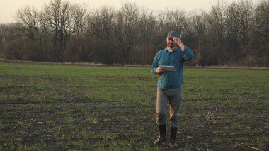 Tarlada elinde tabletle dolaşan bir çiftçi, yerde iş tarımcısı, sebze ve meyve yetiştirme konsepti, kırsal alanda yaşam, istihdam.