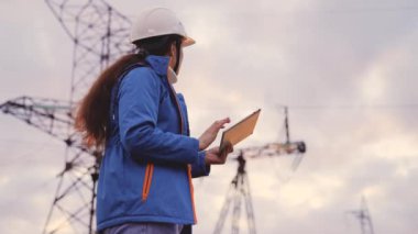 Yüksek gerilim santralinde çalışan bir mühendis gün batımında bir tablette çalışır, elektrik enerjisi tasarımı, endüstri konsepti, modern iş teknolojileri, bir elektrikçi bir cihaz üzerine bir proje okur.
