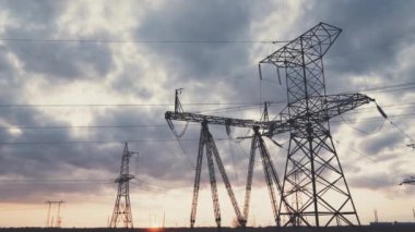 Dönüşüm istasyonu ve yüksek voltaj güç endüstrisi gökyüzünde gün batımında, yüksek kuleleri ve voltaj dağıtım kablolarıyla alt istasyon