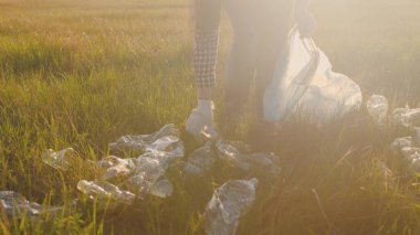 Eldivenli bir kadın gün batımında çöp torbasında çöp topluyor, temiz hava ve toprak ekolojisini koruyor, çevreyi koruyor, dünyayı koruyor, güneşin parlaklığında plastik çöpler.