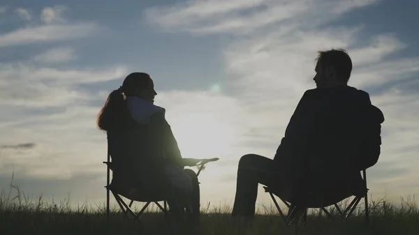 Silhouet van een man en een vrouw die samen naar de zonsondergang kijken in de lucht, hand in hand, familie reizen in de natuur, het concept van een gelukkig leven, op stoelen zitten en ontspannen de dageraad ontmoeten, weekend — Stockfoto