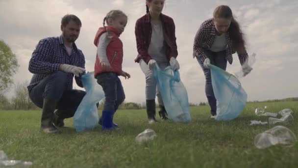 Un niño pequeño con sus padres recoge la basura en un área de recreación del parque, limpieza en grupo del territorio, ecología de la limpieza, recolección de botellas de plástico, residuos, trabajo en equipo, familia feliz y niño — Vídeos de Stock