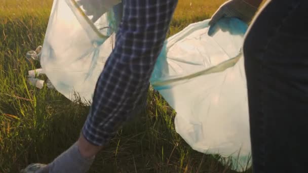 Mensen verzamelen afval, reinigen het milieu van plastic flessen, glazen en servetten, een groep vrijwilligers gooien het afval op de grond met hun handschoenen in een vuilniszak — Stockvideo