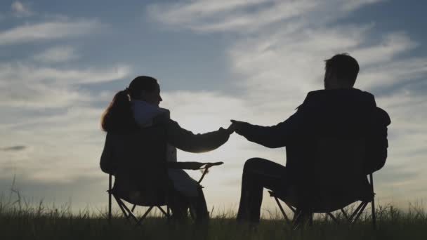 Силуэт мужчины и женщины, видевшие закат вместе в небе, рука об руку, семейные путешествия на природе, концепция счастливой жизни, сидя на стульях и расслабляющие встречи рассвет, выходные — стоковое видео