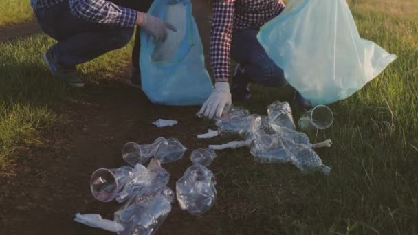 Uma equipa de voluntários recolhe lixo num aterro em sacos de lixo, recolhe garrafas de plástico, as pessoas limpam o planeta verde, põem as coisas em ordem na terra, trabalho de equipa — Vídeo de Stock