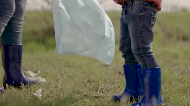 Il bambino raccoglie immondizia in sacchi della spazzatura aiutare i genitori adulti, bambino con la sua famiglia nella pulizia della zona da luoghi di riposo intasati, lavoro di squadra, cancellare il pianeta di sporcizia e blocchi — Video Stock