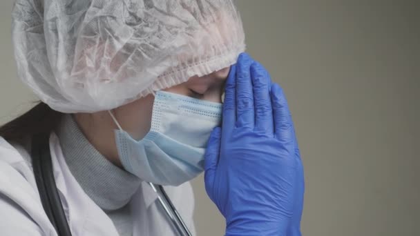 A doctor prays, a medical worker in a white coat, blue gloves, a cap and a mask asks God for help, a nurse is upset at work in a hospital, a doctor worries about the health of patients, fatigue and — Stock Video