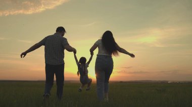 Mutlu bir aile gün batımında küçük bir çocukla sahada koşuyor. Anne, baba ve çocuk koşuyor. Akşamları sahada neşeyle zıplıyorlar.