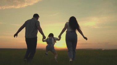 Mutlu bir aile gün batımında küçük bir çocukla sahada koşuyor. Anne, baba ve çocuk koşuyor. Akşamları sahada neşeyle zıplıyorlar.