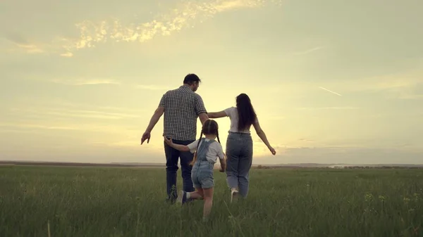 Een gelukkig gezin rent over het veld met een klein kind bij zonsondergang in de lucht, rennende mama, papa en kind springen vrolijk in het veld in de avond, het team reist vrolijk spelend — Stockfoto