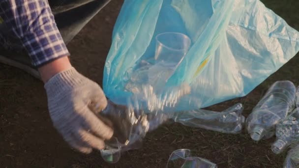 Man hand samlar skräp i en soppåse närbild, befria planeten från en soptipp av plast, flaskor, glasögon, servetter, frivilligt arbete för att rengöra jordytan — Stockvideo