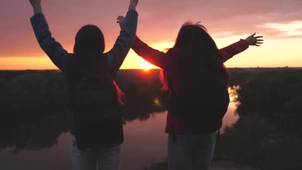 Gelukkig actieve hipster meisjes met rugzakken op hun rug springen bij zonsondergang in de lucht met hun handen omhoog, duizendjarige vrouw reiziger op een hoge berg, bereiken het doel en verheugen zich in de overwinning — Stockvideo