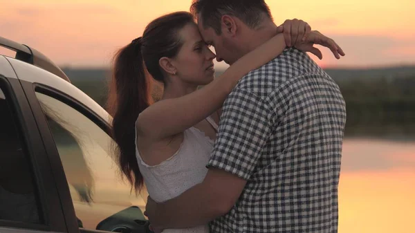 Un hombre y una mujer se abrazan en la orilla de la playa mientras están de pie al atardecer junto al coche, una pareja casada viajando en transporte personal, conociendo el amanecer juntos, relación en un par de —  Fotos de Stock