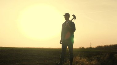 Bir çiftçi gün batımında toprağı kazmak için lastik çizmeli bir kürekle tarlada yürüyor. Tarım, arazi, sebze, meyve, tohum ekme, kazı sezonu.