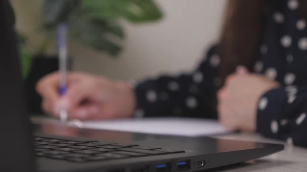 Businesswoman prints a document on a laptop and writes records in a tablet, the work of an office worker in the office at a computer on the table, a girl fills out a job application form, keep records — Stock Video