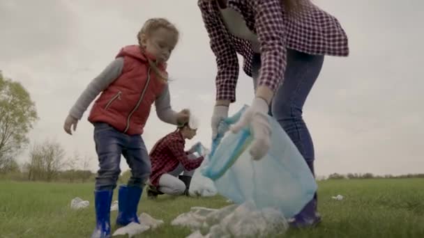 Un petit enfant ramasse les ordures dans une équipe de bénévoles : bouteilles en plastique, lunettes, protéger la planète verte de la pollution avec une équipe familiale de groupe, vivre dans une nature propre — Video
