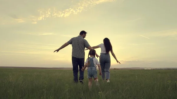 A happy family runs across the field with a small child at sunset in the sky, running mom, dad and kid are jumping cheerfully in the field in the evening, the team is traveling cheerfully playing — Stock Photo, Image