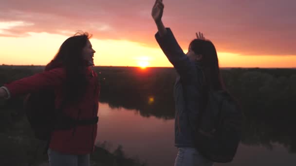 Glückliche aktive Hipster-Mädchen mit Rucksäcken auf dem Rücken, die bei Sonnenuntergang mit erhobenen Händen in den Himmel springen, Millennial-Reisende auf einem hohen Berg, erreichen das Ziel und jubeln über den Sieg — Stockvideo