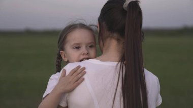 Anne kucağında küçük bir çocuk taşıyor, annesiyle birlikte yeşil çimenlerde yürüyor, mutlu bir aile kavramı, annelik sevinci, bir kız dadıya sarılıyor.