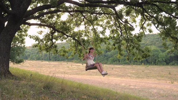 Een volwassen meisje zwaaiend op een schommel vastgebonden aan een boom in de natuur, zwevend in de lucht in de wind en lachend, het concept van een gelukkig leven — Stockfoto